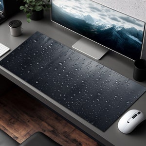 May include: A black desk mat with a water droplet pattern. The mat is on a gray desk with a computer monitor, a mouse, and a cup.