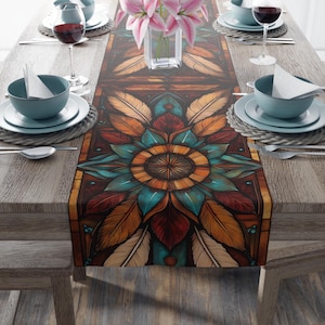 May include: A brown, teal and gold table runner with a geometric pattern of feathers and a mandala design. The runner is on a wooden table with place settings.