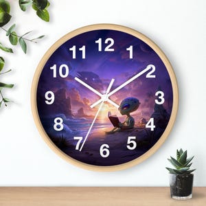 Puede incluir: Reloj de pared redondo con marco de madera clara. La esfera del reloj presenta un extraterrestre leyendo un libro en una playa con un fondo de puesta de sol. Los números y las manecillas blancas indican la hora.