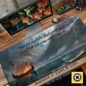 May include: A desk mat with a scenic landscape featuring a burning Viking ship sailing on a lake. The background includes mountains and a cloudy sky. The text "Fear not death for the hour of your doom is set and none may escape it." is written in black on the mat. The text "Norse Proverb" is written in smaller font below the quote. The mat is available in various styles and sizes to fit any desk.