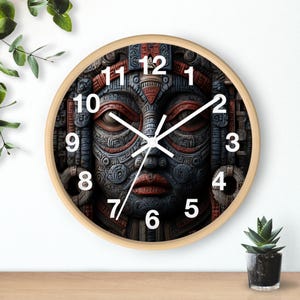 May include: A round wall clock with a light wood frame. The clock face features a detailed, stylized face with red and blue accents. White hands indicate the time. The clock is on a wooden surface with a small potted plant.