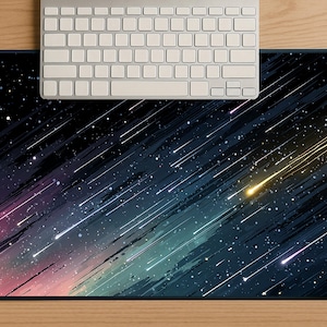 May include: A rectangular mouse pad with a celestial design featuring a dark blue background with streaks of color and white stars. A silver keyboard rests on the top of the mouse pad, which is on a wooden surface.