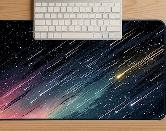 May include: A rectangular mouse pad with a celestial design featuring a dark blue background with streaks of color and white stars. A silver keyboard rests on the top of the mouse pad, which is on a wooden surface.