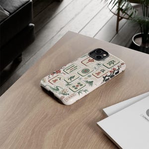 May include: A smartphone case featuring a cream-colored background with a decorative pattern of Mahjong tiles, red cherry blossom branches, and green bamboo stalks. The design includes various Chinese characters and circular symbols in red and green.