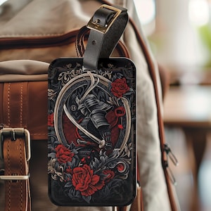 Könnte beinhalten: Ein schwarzes Gepäckanhänger mit einer Grafik eines Samurai-Kriegers in einem roten und schwarzen Blumendesign. Der Anhänger hat ein schwarzes Lederband mit einer goldenen Schnalle.