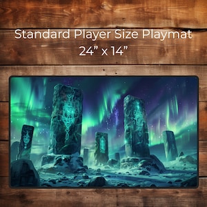 Puede incluir: Un tapete de juego verde y azul con un paisaje de fantasía que presenta altos pilares de piedra con runas brillantes y un cielo estrellado con auroras boreales verdes. El tapete de juego mide 61 cm por 36 cm.