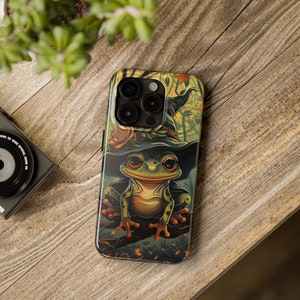 May include: A green frog wearing a witch's hat with orange and yellow flowers. The frog is sitting on a branch with green leaves and brown bark. The background is a blurry image of a forest.