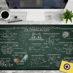 May include: A green chalkboard-style desk mat with the text "The Physics of Cats" and various cat-related scientific diagrams. The mat also features the text "Available in Many Styles/Sizes". A coffee cup, pencil, and computer are visible.