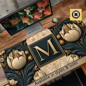 May include: A rectangular desk mat featuring a large gold letter M centred within a dark square frame. The design includes cream-coloured floral blossoms and dark teal foliage patterns on a beige background with ornate scrollwork details.