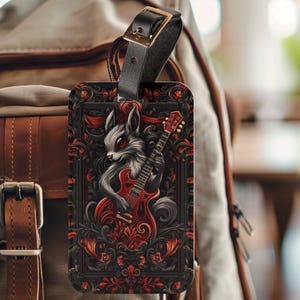 May include: A luggage tag featuring a black and white illustration of a creature playing a red electric guitar. The illustration is surrounded by a red and black floral design.