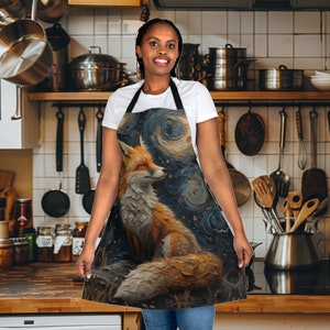 Puede incluir: Un delantal negro con un diseño de zorro colorido y noche estrellada. El delantal tiene tirantes ajustables y un bolsillo grande.