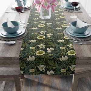 May include: A green and white floral table runner with a repeating pattern of flowers and leaves. The runner is on a wooden table with place settings on either side.