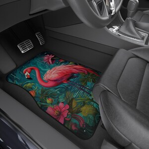 May include: A pink flamingo with a tropical floral design on a car floor mat. The mat is teal blue with green leaves and pink flowers.