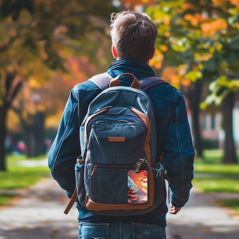 May include: A blue backpack with a brown leather trim and a luggage tag featuring a colorful illustration of a Japanese temple and a red moon.