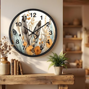 May include: A round wall clock with a black frame. The clock face features a floral design with feathers, flowers, and foliage in shades of orange, gray, and blue. The clock hands are black.