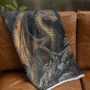 Pu&ograve; includere: Una coperta in peluche con un'illustrazione dettagliata di un drago verde e oro con le ali spiegate. Il drago &egrave; appollaiato su una scogliera rocciosa su uno sfondo scuro.