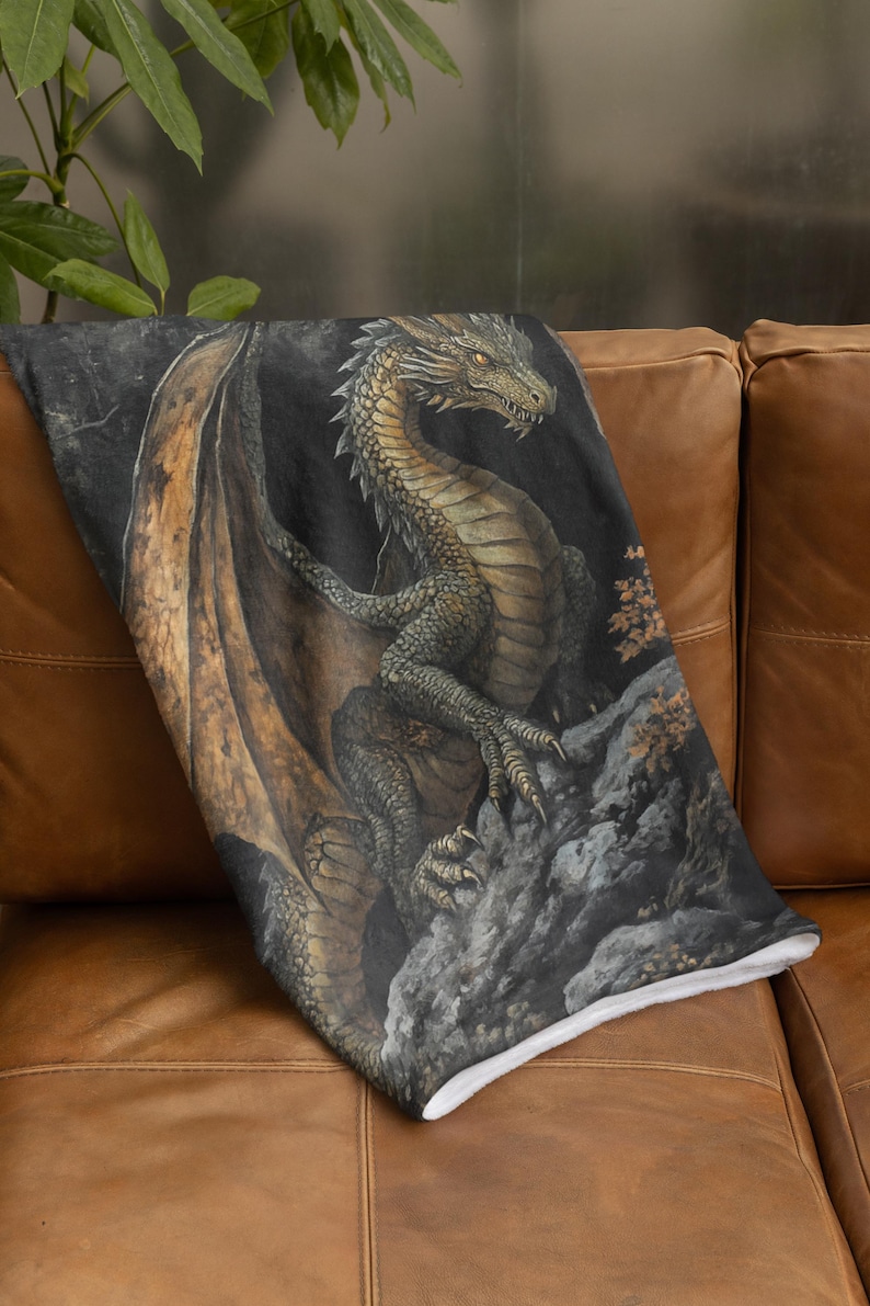 Pu&ograve; includere: Una coperta in peluche con un'illustrazione dettagliata di un drago verde e oro con le ali spiegate. Il drago &egrave; appollaiato su una scogliera rocciosa su uno sfondo scuro.