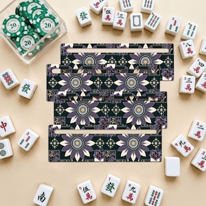 Può includere: Quattro supporti rettangolari in legno per tessere del mahjong con uno sfondo scuro e un motivo floreale ripetitivo viola e crema. Ogni supporto presenta una fessura orizzontale per le tessere, circondato da tessere del mahjong e fiches da poker.