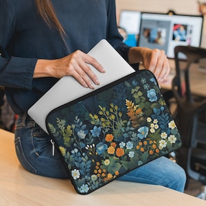 May include: A laptop sleeve with a dark background and a colorful floral pattern. The flowers are in shades of blue, yellow, orange, and white. The sleeve is made of a soft, durable material and is perfect for protecting your laptop.