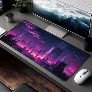 Peut inclure: Tapis de bureau rectangulaire avec un design de paysage urbain futuriste en violet, rose et bleu. L'&oelig;uvre repr&eacute;sente une ligne d'horizon avec de grands b&acirc;timents, des n&eacute;ons et un ciel dramatique. Une souris et un clavier blancs sont visibles.