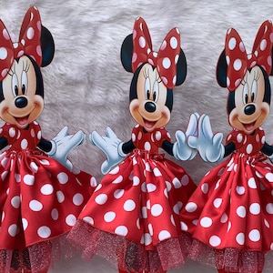May include: Three red and white polka dot Minnie Mouse centerpieces with tulle skirts. Each centerpiece is on a red stand.