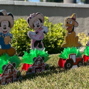 以下が含まれることがあります： ミッキーマウス、ミニーマウス、ドナルドダック、グーフィーをフィーチャーした、農場をテーマにしたセンターピース4つ。各センターピースには、キャラクターの切り抜き、緑の草のようなベース、赤い納屋とトラクターが含まれています。