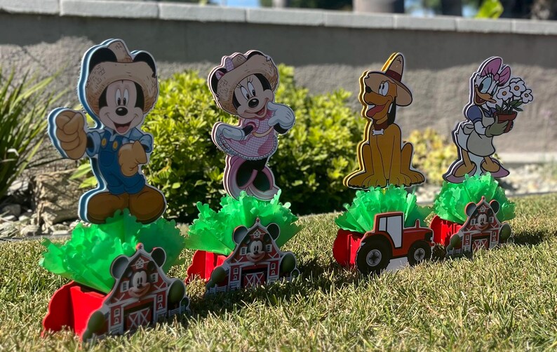 以下が含まれることがあります： ミッキーマウス、ミニーマウス、ドナルドダック、グーフィーをフィーチャーした、農場をテーマにしたセンターピース4つ。各センターピースには、キャラクターの切り抜き、緑の草のようなベース、赤い納屋とトラクターが含まれています。