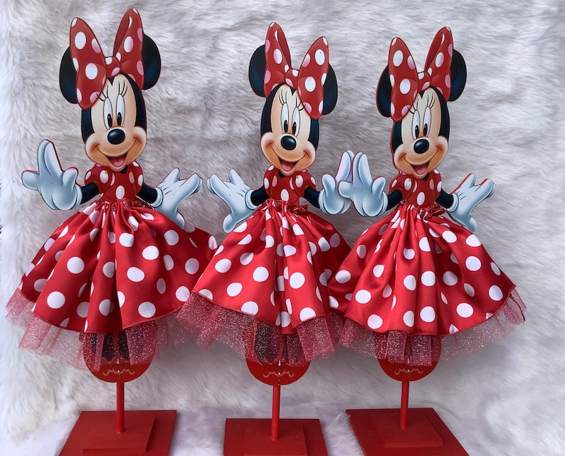 May include: Three red and white polka dot Minnie Mouse centerpieces with tulle skirts. Each centerpiece is on a red stand.