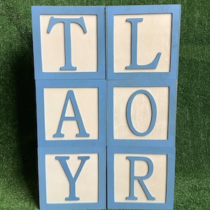 May include: Six blue wooden blocks with white letters spelling out the name "TAYLOR".