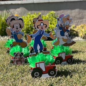 以下が含まれることがあります： ミッキーマウス、ドナルドダック、グーフィーのキャラクターをフィーチャーした、農場をテーマにしたセンターピースが4つ。各センターピースには、緑のふわふわのベース、赤いトラクター、キャラクターの切り抜きが含まれています。