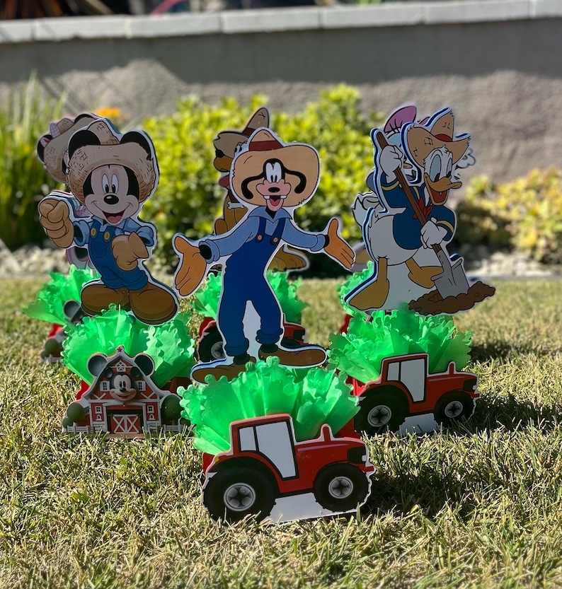 以下が含まれることがあります： ミッキーマウス、ドナルドダック、グーフィーのキャラクターをフィーチャーした、農場をテーマにしたセンターピースが4つ。各センターピースには、緑のふわふわのベース、赤いトラクター、キャラクターの切り抜きが含まれています。