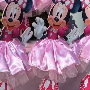 May include: Two pink and white polka dot Minnie Mouse centerpieces with red shoes and a white tulle skirt.