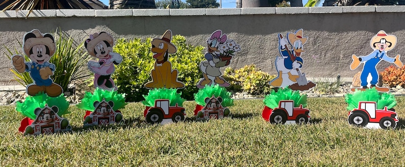 以下が含まれることがあります： ミッキーマウス、ドナルドダック、グーフィー、プルートをフィーチャーした、農場をテーマにしたセンターピース6個セット。各センターピースには、キャラクターの切り抜き、緑色のベース、赤いトラクターが含まれています。