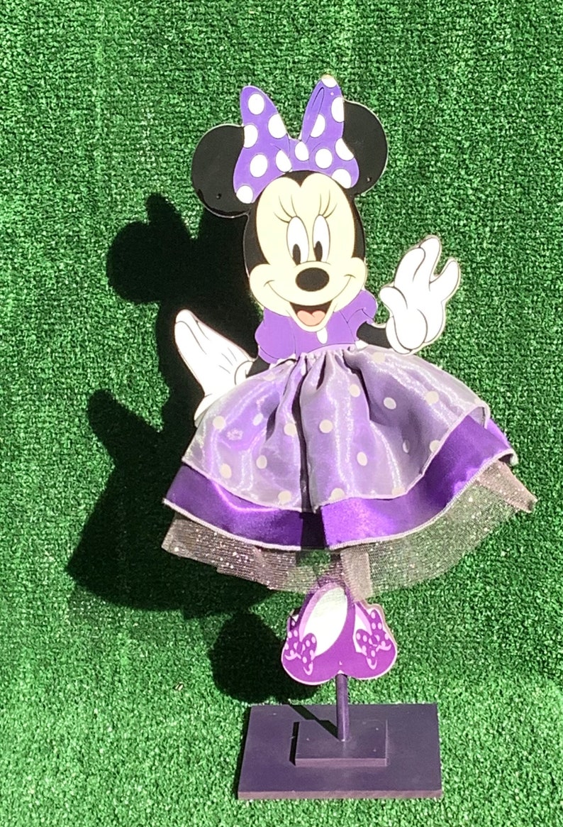 May include: Purple Minnie Mouse figurine with a white polka dot dress and bow. The figurine is standing on a purple base.