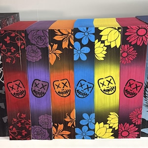 May include: A collection of colorful, wooden decorative blocks. Each block features a unique design, including floral patterns, a grinning mask, and a spiderweb. The blocks are painted in a gradient of colors, including red, purple, orange, blue, yellow, and pink.
