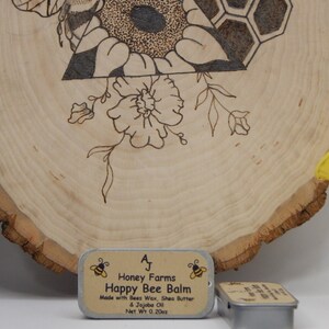 May include: A wooden slice with a burned bee and floral design, with a small tin of Happy Bee Balm. The balm is made with beeswax, shea butter, and jojoba oil, net weight 0.20oz.
