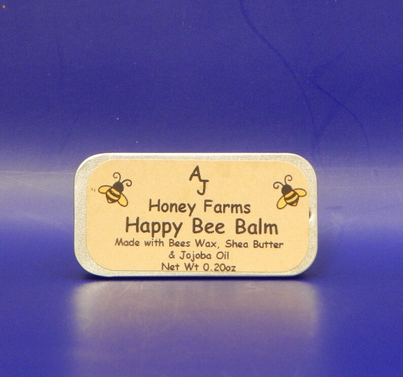 May include: A rectangular tin of Happy Bee Balm from Honey Farms, with a light brown label and a blue background. The label features two cartoon bees and the text "Happy Bee Balm." The net weight is 0.20 oz.