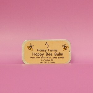 May include: A rectangular tin of Happy Bee Balm from Honey Farms, with a light brown label and a pink background. The label features two cartoon bees and the text "Happy Bee Balm." The net weight is 0.20oz.