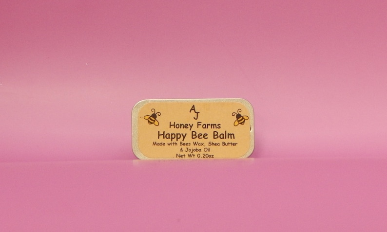 May include: A rectangular tin of Happy Bee Balm from Honey Farms, with a light brown label and a pink background. The label features two cartoon bees and the text "Happy Bee Balm." The net weight is 0.20oz.