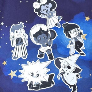 May include: A selection of grayscale cartoon stickers depicting different characters. The stickers include a character in an astronaut helmet, a character in a witch hat, and other stylized figures. The background is a dark blue with white stars.