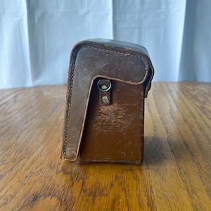 May include: A brown leather camera case with a flap and a metal clasp.