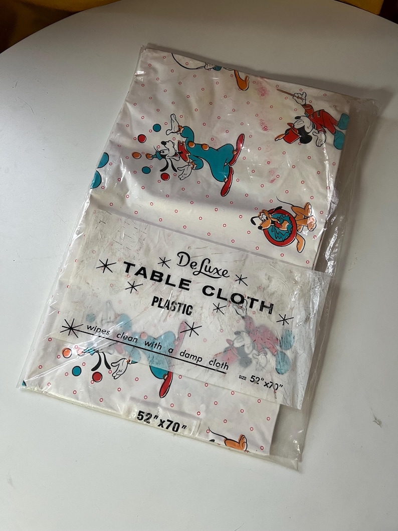 Puede incluir: Un mantel de pl&aacute;stico vintage con Mickey Mouse y sus amigos en un dise&ntilde;o l&uacute;dico. La tela blanca tiene un patr&oacute;n de lunares rojos y personajes de dibujos animados. El paquete dice "Deluxe Table Cloth" y mide 132cm x 178cm.