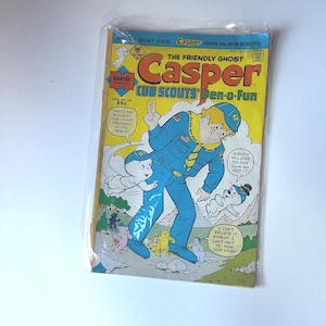以下が含まれることがあります： 保護プラスチックケースに入った、ヴィンテージコミック「Casper the Friendly Ghost」。表紙には、キャスパーと他の漫画のキャラクターがカブスカウトをテーマにしており、「Cub Scouts Den-o-Fun」と書かれています。