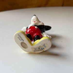 Puede incluir: Una figura de cer&aacute;mica de Mickey Mouse, con cabeza y orejas negras, guantes blancos, pantalones cortos rojos y zapatos amarillos. La base est&aacute; marcada "Disney Japan".