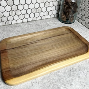 May include: A large, rectangular wooden serving tray with a light brown wood finish. The tray has a slightly raised edge and a smooth surface.