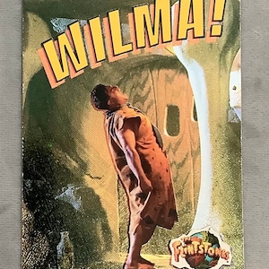 May include: A vintage trading card featuring a cartoon character from The Flintstones. The character is a man with brown skin, wearing a brown and orange outfit. He is looking up and yelling "WILMA!" The card has a gold background and a logo for The Flintstones.