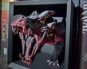 Könnte beinhalten: Eine schwarze Drachenskulptur mit offenem Maul, scharfen Zähnen und langer Zunge, eingerahmt in einer schwarzen Box. Die Details des Drachen sind mit roten Akzenten hervorgehoben. Die Skulptur ist ein dekoratives Objekt.