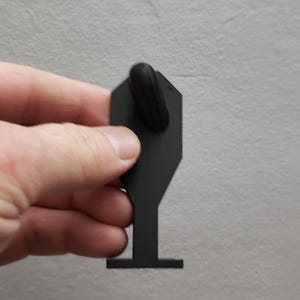 May include: Black plastic stand with a rounded top and a flat base. The stand is designed to hold a small object.