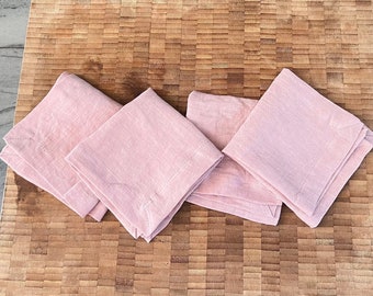 Könnte beinhalten: Vier rosa Leinen Servietten gefaltet und auf einem Holzbrett gestapelt.