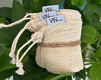 Könnte beinhalten: Drei beigefarbene Netztaschen für Lebensmittel mit einem weißen Kordelzug und einem weißen Etikett mit der Aufschrift "VASI STUDIO" auf jeder Tasche.